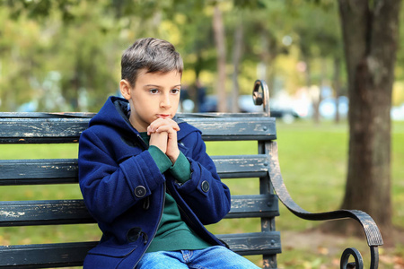 在公园里祈祷坐在长椅上的小男孩