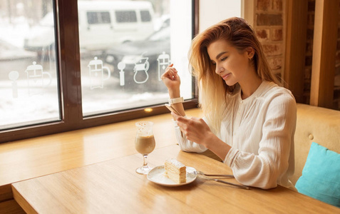 女孩坐在一个咖啡馆，使用智能手机，在手机上键入