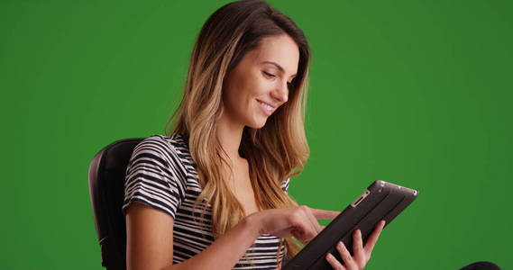 年轻的女性千禧年坐在椅子上使用平板电脑在绿色屏幕上