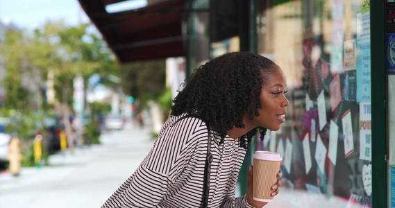 可爱的黑人妇女在条纹顶部喝咖啡, 看着窗口显示