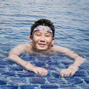 阳光明媚的日子里, 亚洲男孩戴着护目镜, 在游泳池里游泳