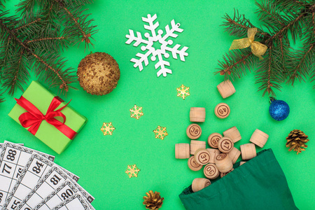 棋盘游戏。木莲花桶与袋和游戏卡的游戏在, 圣诞冷杉树枝, 锥, 玩具球, 雪花和礼品盒在绿色背景。顶视图