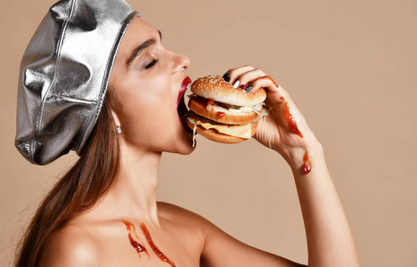 妇女举行汉堡三明治与番茄酱与饥饿的嘴在浅棕色背景