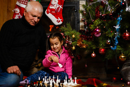 爷爷教孙女在装饰过的壁炉和圣诞树附近下棋