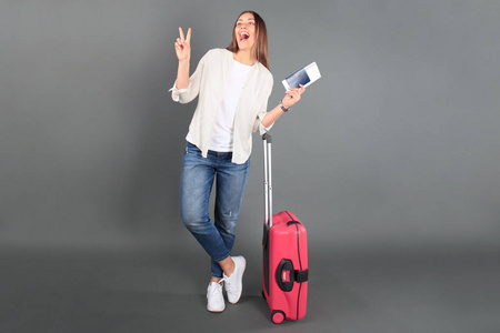 年轻的旅游女孩在夏天休闲服, 红色手提箱, 护照, 在灰色背景隔离的票