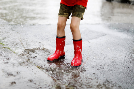 穿红色雨鞋的小孩跳进水坑.关门了孩子玩水溅的乐趣.