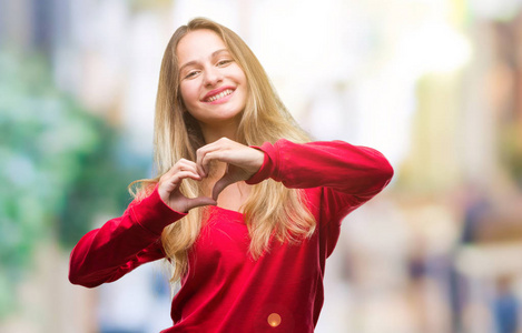 年轻美丽的金发碧眼的女人穿着红色毛衣在孤立的背景微笑着在爱中显示心脏符号和形状与手。浪漫的概念