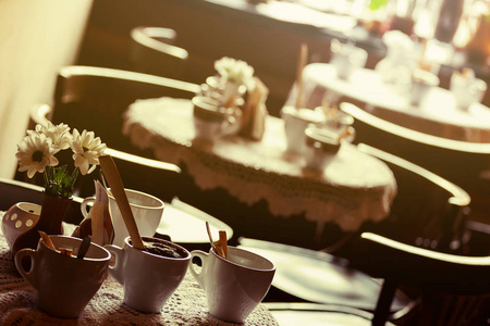 静物。白色的瓷杯子和一个花瓶花站着一个棕色的咖啡厅大厅的白色桌布的桌子上