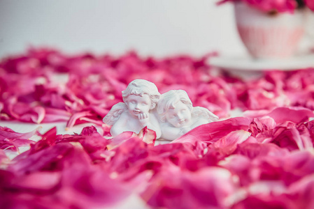 在白色背景上的石膏的两个古色古香的小可爱的天使的雕像与粉红色紫色牡丹花瓣。爱, 浪漫, 情人节的概念。关闭, 选择性的焦点。复制