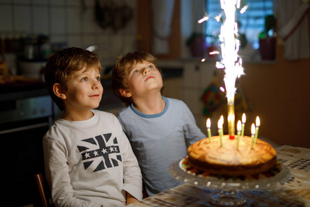 两个漂亮的孩子，学龄前的小男孩，庆祝生日和自制烤好的蛋糕，室内吹蜡烛。兄弟姐妹的孩子的生日聚会。关于礼物的快乐双胞胎