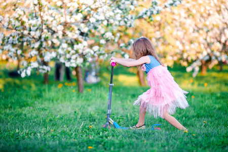 在春日盛开的苹果树木园在滑板车上开心的小女孩