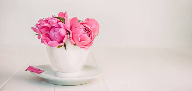 关闭浅粉色牡丹花花束在一个装饰杯和茶托上的白色木桌。爱。礼品问候赞美背景。复古调理。宽横幅。选择性对焦。复制空间