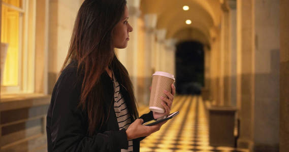 希普斯特女孩拿着咖啡, 同时在建筑物走廊用手机发短信