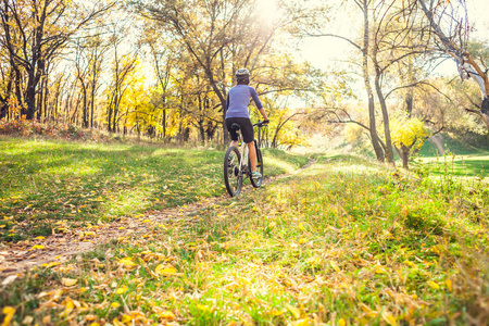 那个带着背包的女孩在秋季公园里骑自行车。苗条的女人在大自然中训练。在森林里运动。游客骑在泥土小径上。骑自行车旅行