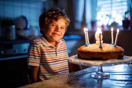 可爱快乐金发碧眼的小小孩男孩庆祝他的生日。在自制烤好的蛋糕，室内吹蜡烛的孩子。生日派对学校儿童家庭庆祝 6 年