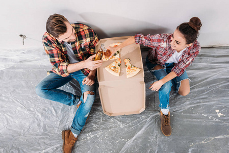 在新公寓的地板上, 年轻夫妇在地板上叮当作响的啤酒瓶和吃比萨饼的头顶上的看法