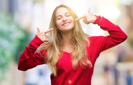 年轻美丽的金发女子穿着红色毛衣在孤立的背景微笑自信地显示和指着手指牙齿和嘴。健康理念