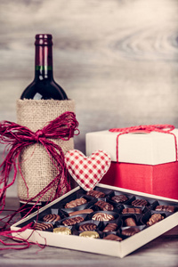 红酒瓶, 一盒巧克力和装饰由红色心脏在木桌上的礼物。情人节庆祝概念。复制空间