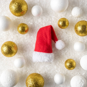 金色和白色闪闪发光的球装饰与圣诞老人的帽子在雪中。圣诞节或新年假期背景