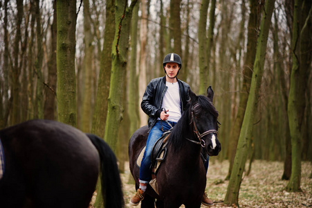 年轻时尚的男人骑着马在秋天的树林