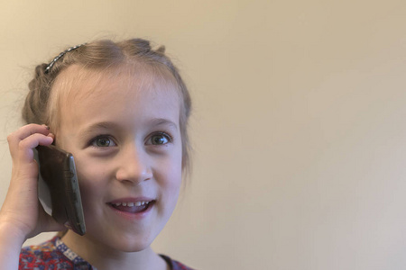 可爱的小女孩正在用手机和微笑说话。女孩谈论智能手机。小孩子使用智能手机。智能手机在手