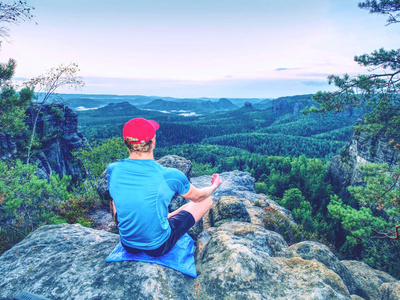 后视图的健身男子沉思瑜伽在美丽的日出岩石。美丽的风景与森林风景。健康和积极的生活方式
