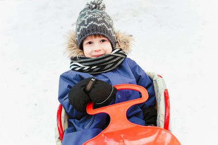 那男孩坐在雪中的雪碟上。穿冬装的孩子在冬天在外面玩耍。男孩在雪地里骑着雪桑拿