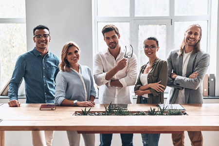 一群快乐微笑的商务人士团队在木桌在创造性的现代办公室工作室摆姿势