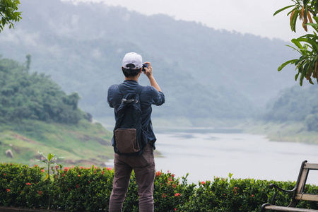 后面的年轻亚洲旅行者男子拍照与手机户外风景背景。生活方式和休闲理念