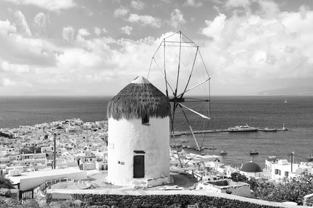 在希腊米科诺斯岛上的海上风车。在多云的天空上的海景风车。白色建筑与风帆和稻草屋顶与尼斯建筑学。在岛上的暑假。地标和吸引力