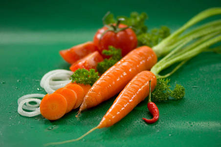 蔬菜洗胡萝卜与顶部, 西红柿, 红色辣椒, 洋葱圈, 欧芹上的绿色模糊的背景