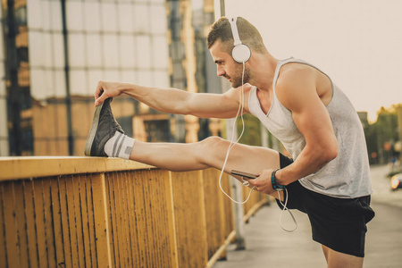 健身训练。年轻的运动员在桥上做伸展运动, 用耳机听音乐。健身运动生活方式理念
