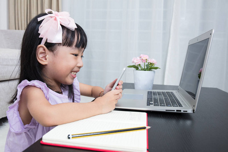 亚洲的中国小女孩忙着阅读手机和笔记本