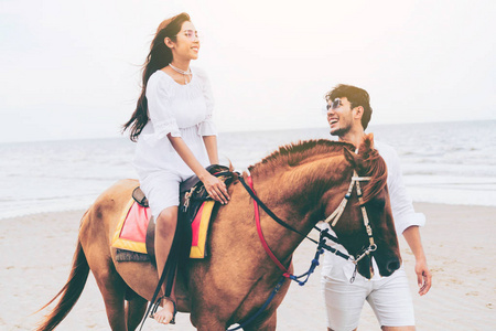 年轻夫妇去蜜月骑马在海滩上的夏天假期