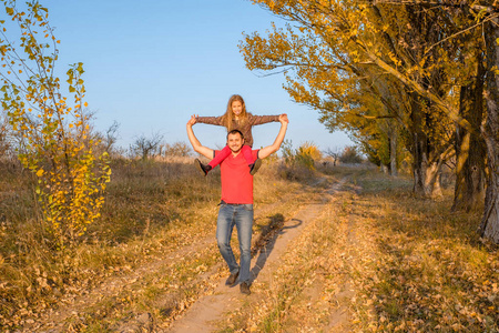 快乐的父亲和女儿在他的肩膀上走着, 笑着在秋天的公园里。幸福的概念一个孩子家庭或单身父亲 parentin