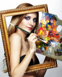 青年女画家在金框与颜色托盘和油漆