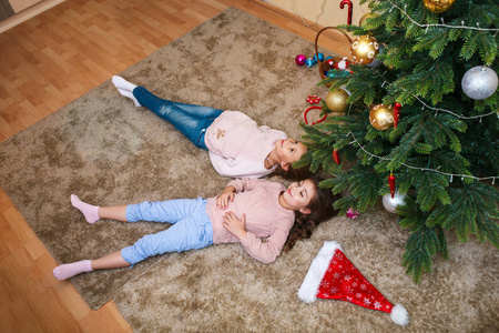 圣诞节快乐有趣的孩子姐妹躺在圣诞树下, 玩得很开心