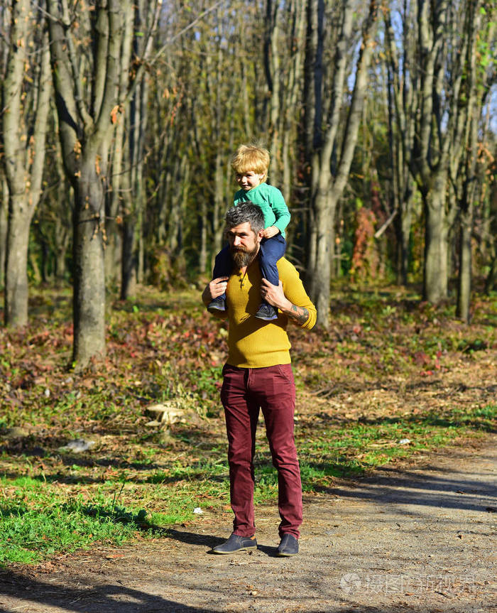 爸爸把小孩子背在公园里.爸爸和儿子在户外享受阳光明媚的一天.