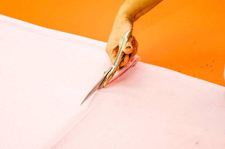 妇女的手削减粉红色的织物与剪刀