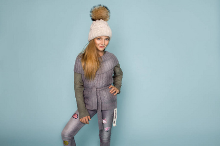 可爱的小女孩穿着冬衣, 帽子和冬天夹克, 站在蓝色的背景