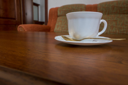一个白色的杯子, 上面有一个茶托和一个勺子, 站在沙发附近的木桌上