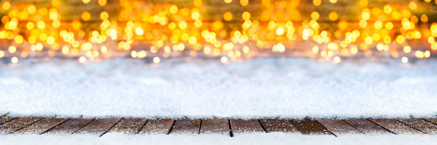 空木板地板在圣诞节雪在明亮的灯光前金色温暖的 bokeh 宽全景圣诞节背景