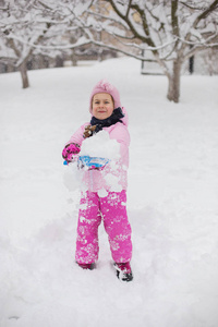 这孩子在冬天玩雪。一个穿着鲜艳夹克头戴针织帽子的小女孩, 在冬季公园里捕捉雪花过圣诞节。孩子们在被雪覆盖的花园里玩耍和跳跃