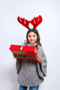愉快的小微笑的女孩与圣诞礼物盒。圣诞节的概念。微笑的滑稽的女孩在鹿角在演播室
