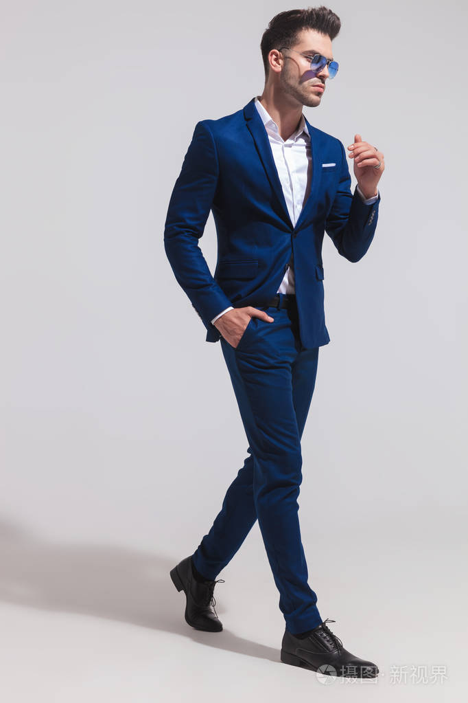 一个穿着蓝色西装的时尚优雅男人的侧视图走在灰色的背景照片-正版