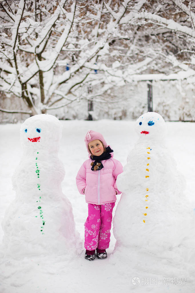 这孩子在冬天玩雪。一个穿着鲜艳夹克头戴针织帽子的小女孩, 在冬季公园里捕捉雪花过圣诞节。孩子们在被雪覆盖的花园里玩耍和跳跃