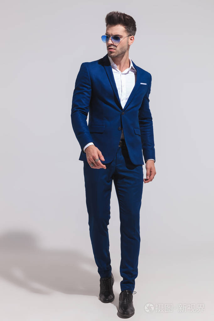 戏剧性的年轻性感优雅的男人在西装和太阳镜是走向前, 看着一边