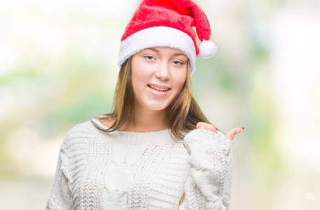 年轻美丽的白人妇女戴着圣诞节帽子在孤立的背景微笑与快乐的脸看和指向侧与拇指向上