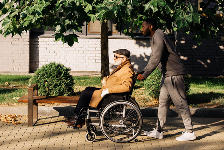 坐在轮椅上的高级残疾男子和在街上骑行的护士的侧视图