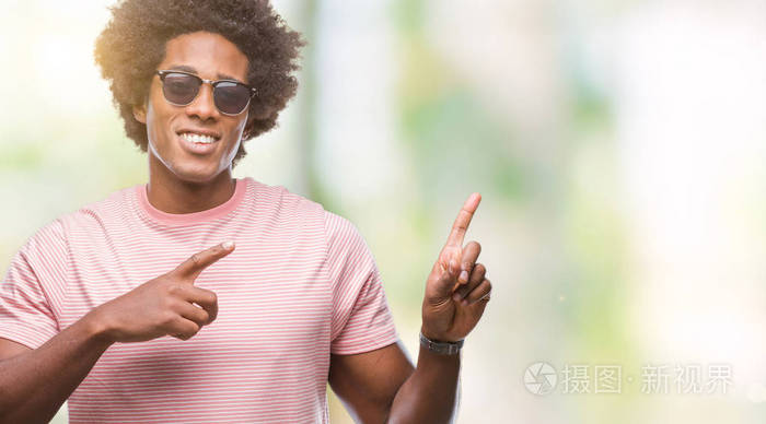 美国黑人戴着太阳镜在孤立的背景下微笑着看着两只手和手指指向侧面的